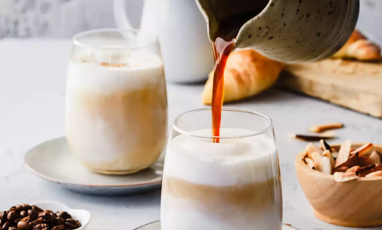 Picture - Coconut Vanilla Latte med kremet hvitt skum og gyllen kaffe i glass, servert på lyse asjetter med kaffebønner, skjeer og en keramikkkanne